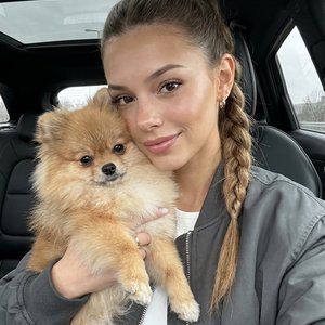 Вертикальное cinematic selfie, съёмка на iPhone front camera 28mm lens, close-up crop, камера вытянута на уровне лица внутри автомобиля. Девушка сидит на переднем сиденье машины с панорамной крышей, корпус слегка развёрнут в сторону окна. Она смотрит прям