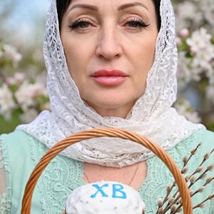 Потрясающий портрет крупным планом светлокожей женщины с эффектным макияжем, сосредоточенной и смотрящей прямо на зрителя. У нее темные волосы, эффектная крылатая подводка для глаз, длинные темные ресницы, идеально очерченные брови и полные блестящие розо