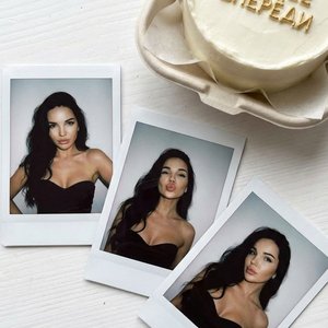 Create a portrait without changing your facial features. Three polaroid photographs spread out on a white table. There is a bento cake with the golden inscription "ВСЕ ЛУЧШЕЕ ВПЕРЕДИ."  photo of a woman with loose voluminous hair on one side without a par