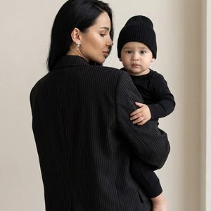 Use the uploaded photo as the exact face reference and keep the faces identical (eyes, nose, lips, skin tone, hairstyle, proportions). Recreate the same composition exactly: a stylish woman standing with her back slightly turned to the camera while holdin