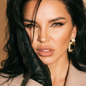 transfer the face and human parameters from my reference photo, preserve identity 100%. Ultra-realistic close-up, centered, eye-level. Black leather glove pressed to cheek. Expression intense feline squint, lips softly parted. Hair voluminous, brushed bac