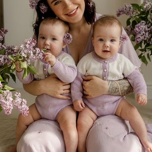 Ultra-realistic professional photo of a young mother with her two identical twin baby girls, 8 months old. They are sitting together on a soft cream linen rug. Mother weighs 65 kg, has a slim but naturally soft body type — not skinny, healthy and feminine