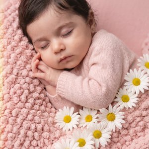 Professional studio portrait, tight close-up shot from a gentle 45° overhead angle; sleeping baby lying on their side on a plush pink chenille “popcorn” blanket; eyes closed (no eye contact), lips closed and relaxed, mouth neutral, peaceful expression; bo