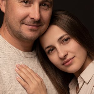 Лица точь в точь ,не меняя цвет волос,не меняя цвет глаз,в студии на темном фоне. Мужчина  одет в светлый свитер. У него доброе лицо, он смотрит в камеру. Женщина одета в светлую рубашку. У нее выразительные глаза, полные нежности, она склонила голову на 