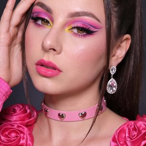 A girl poses in a close-up portrait with her head tilted slightly to the left and her gaze directed firmly toward the camera, expressing a confident and intense look. Her right hand is raised to the side of her face, fingers gently resting on her temple a