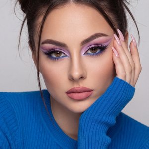 A girl is posed in a close-up portrait, leaning slightly forward. Her right hand supports the right side of her face, with fingers elegantly touching her cheek and chin, showcasing long, manicured nails in a light color. The left arm is bent with the slee