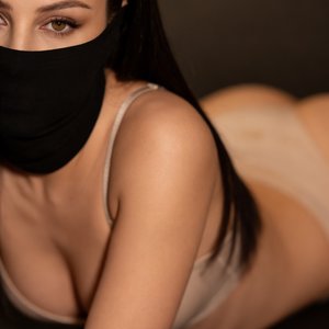 A girl is posed lying on her stomach with her upper body slightly raised and turned toward the camera. Her left arm is bent at the elbow, resting close to her body, and her right arm is mostly out of frame, suggesting a relaxed, almost casual posture. She