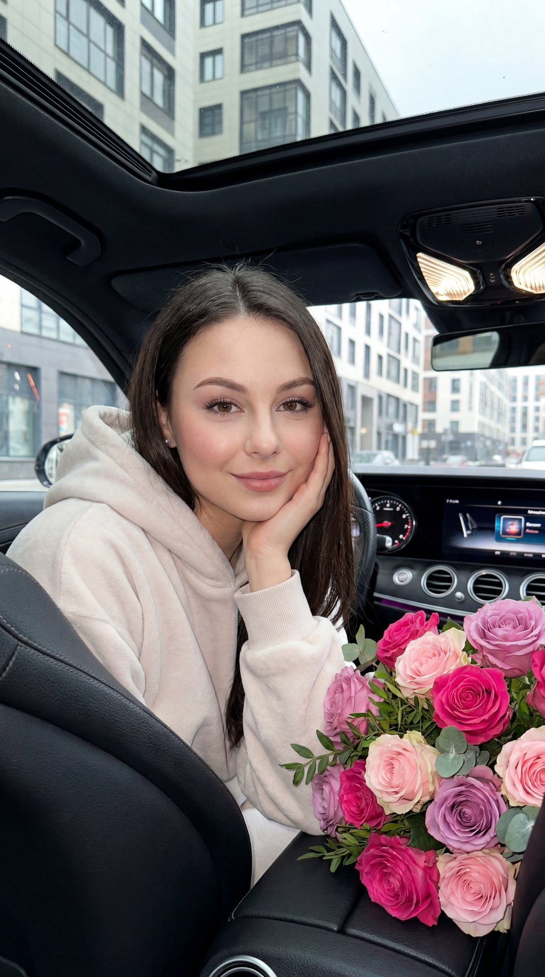 Professional photo of a woman sitting in the interior of a modern car, mid-shot, 3/4 viewing angle from the front passenger seat, slightly lowered; she is turned towards the camera in a relaxed position, left forearm resting on the door, left hand gently 