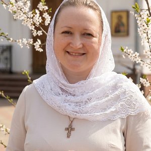 Точное воспроизведение внешности с загруженной фотографии: форма лица, особенности глаз, носа, губ, цвет волос темно русый, идентичная структура лица, максимальное сходство. Фотореалистичный портрет по пояс, женщина стоит на фоне православной церкви в пас