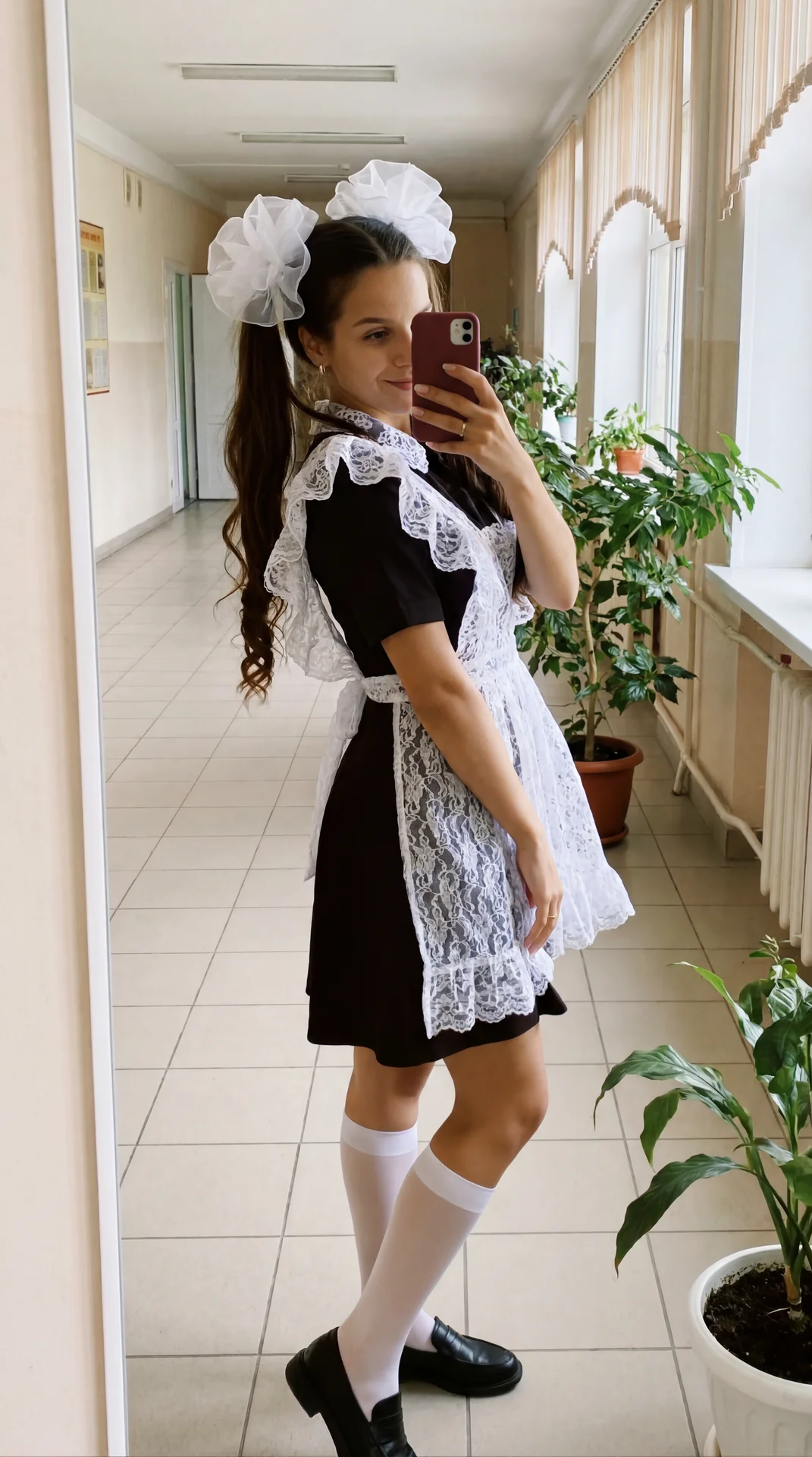 Создай Максимально реалистичное mirror selfie фото в школьном коридоре, одна девушка-выпускница стоит напротив большого зеркала и фотографирует себя на телефон. На ней советская школьная форма: приталенное чёрное платье с короткими рукавами и белый очень 