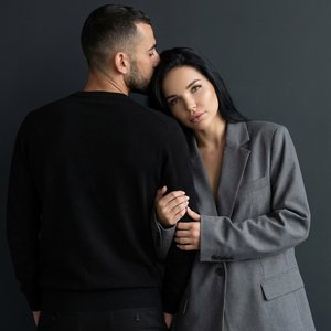 Использовать входящее фото только как источник лиц, кожи, волос и пропорций людей. Полностью и строго воссоздать сцену как в референсе без изменений. Вертикальный формат 9:16, фотореализм. Минималистичная fashion-сцена в студийном стиле на фоне тёмной мат