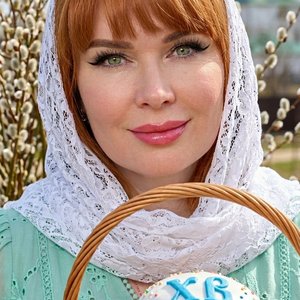 Потрясающий портрет крупным планом светлокожей женщины  сосредоточенной и смотрящей прямо на зрителя. У нее рыжие  волосы, , длинные темные ресницы,. Ее глаза очаровательного светло-зеленого цвета. На ней нежный белый кружевной платок, обрамляющий лицо, и