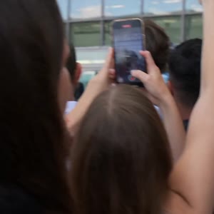 Style: Ultra realistic mass celebrity entry scene. Single continuous shot. Handheld camera from crowd perspective. Natural micro-shake. No cuts. Documentary realism.
Audio: Only natural environment sound — loud crowd cheering, people shouting, rapid camer