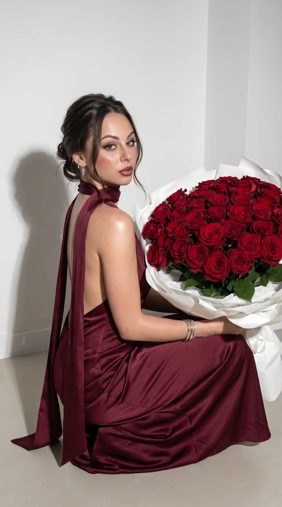 An ultra-realistic young woman gracefully sits next to a huge bouquet of deep red roses wrapped in luxurious white paper, wearing a silk burgundy evening gown with an open back and a long, flowing scarf. She features smooth, glass-like skin, precise, glam