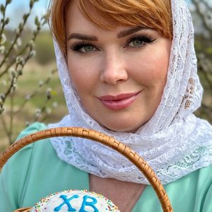 Потрясающий портрет крупным планом светлокожей женщины с эффектным макияжем, сосредоточенной и смотрящей прямо на зрителя. У нее рыжие  волосы, эффектная крылатая подводка для глаз, длинные темные ресницы, идеально очерченные брови и полные блестящие розо