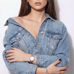 Portrait of a female model, studio shot, professional camera view, eye level, straight angle, medium shot (waist-length), seamless white background; pose: standing straight, torso turned towards the camera, arms crossed in the middle of the torso, left fo