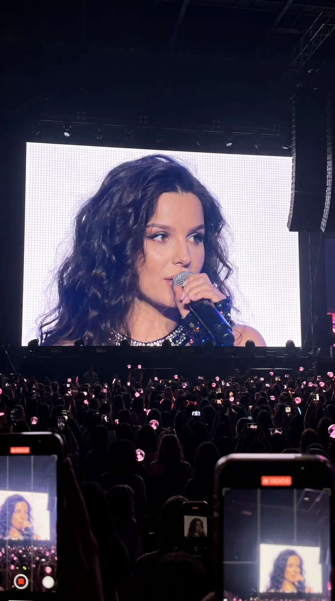 1 portrait photo of a person [MAIN TASK - "REALISTIC JUMBOTRON TRANSLATION AT A K-POP CONCERT"] Transform the person in the photo into a famous K-pop artist performing at a sold-out concert. The final result should look like this: a real fan secretly take