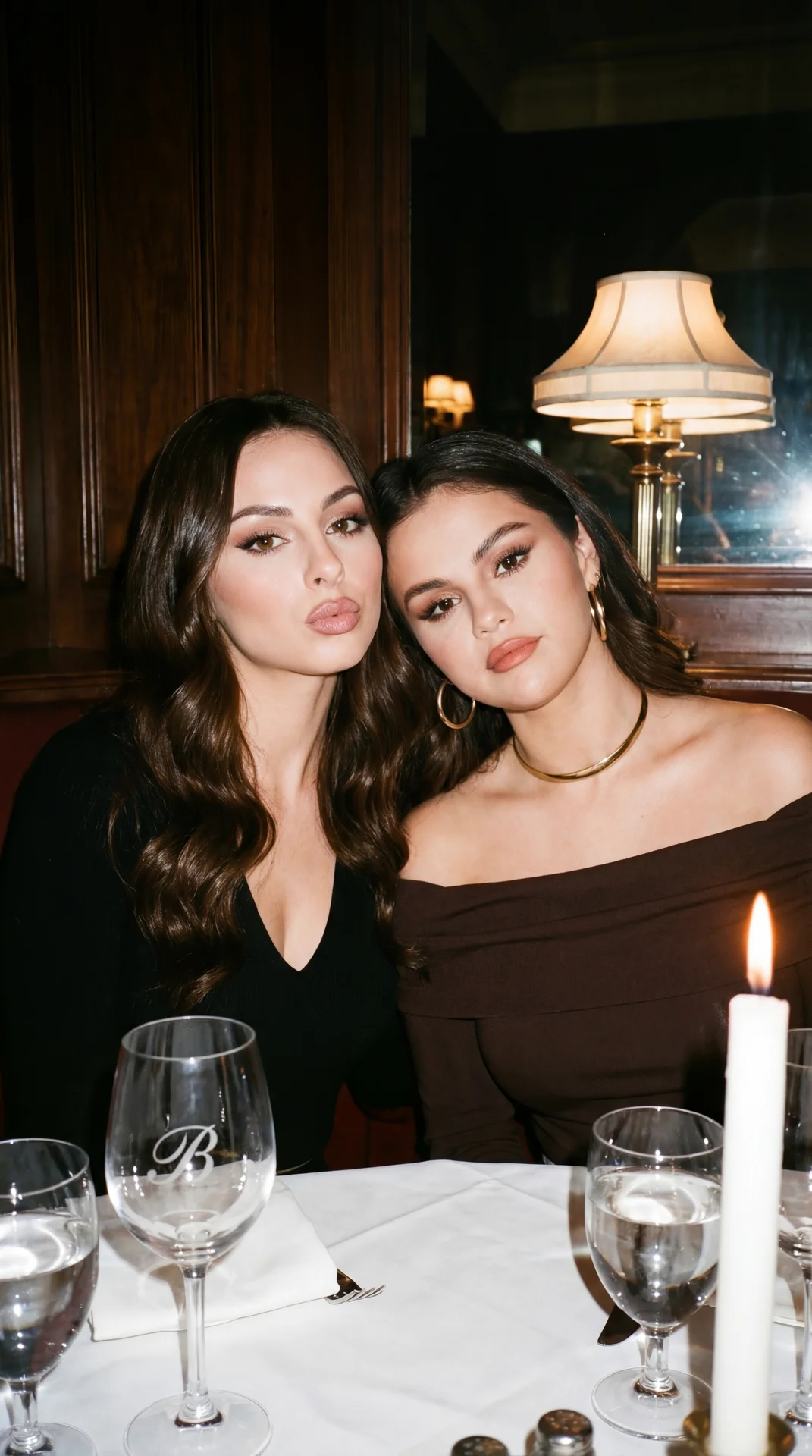 A girl sitting at a table in a restaurant is posing intimately, cheek to cheek with a second girl. The picture was taken at chest level, the camera is exactly at eye level. Both have slender figures. The first girl leans slightly forward, her torso is tur