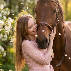 Ultra-realistic cinematic photography of a young woman with long straight light brown hair. She is wearing a soft pink lace dress with a delicate ribbon belt. She is standing in a tender embrace with a majestic brown bay horse, gently resting her cheek ag