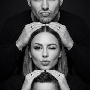 Create a high-contrast black-and-white studio portrait of a three-person family stacked vertically in a perfectly centered totem-pole composition, faces closely matching the reference image identities, preserving exact facial structure,
proportions, skin 