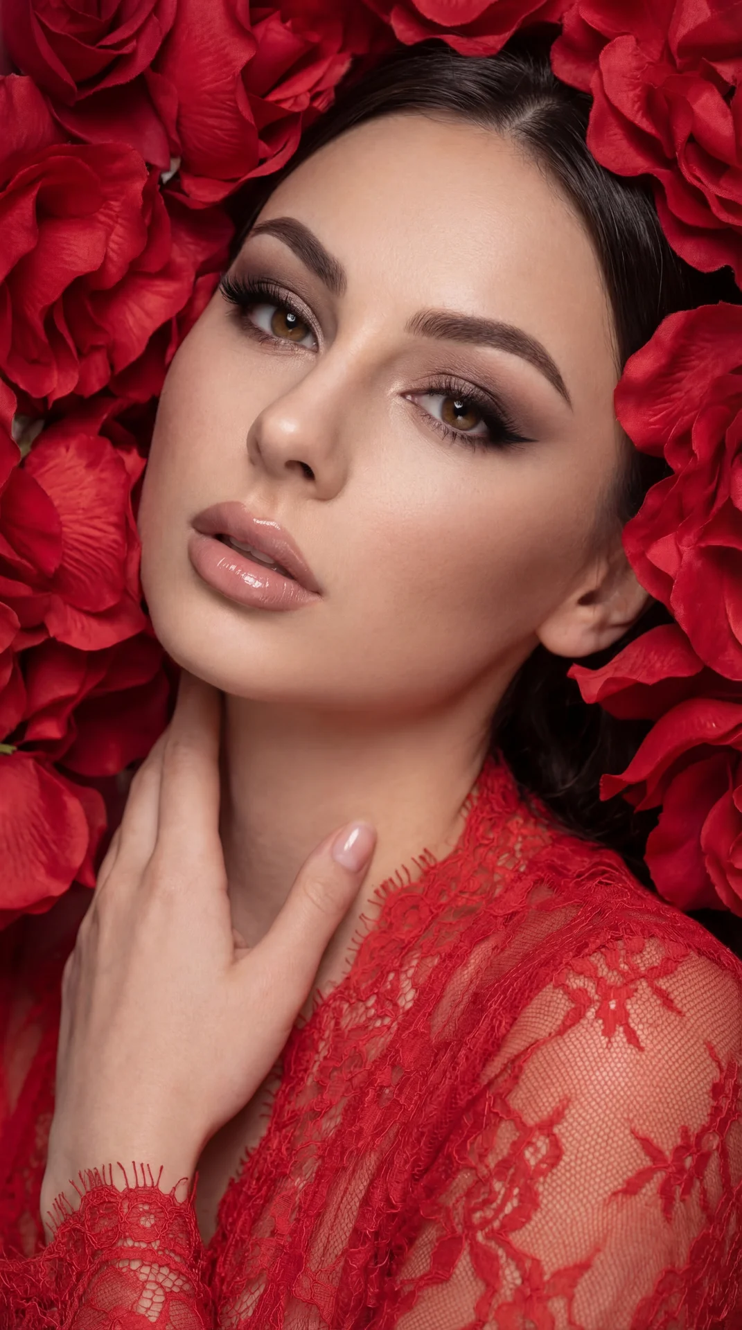 A girl is surrounded by vibrant red flower petals that frame her face closely, creating an immersive and dramatic floral backdrop. She is positioned leaning slightly backward, with only her upper body visible in the frame. Her right hand is gently touchin