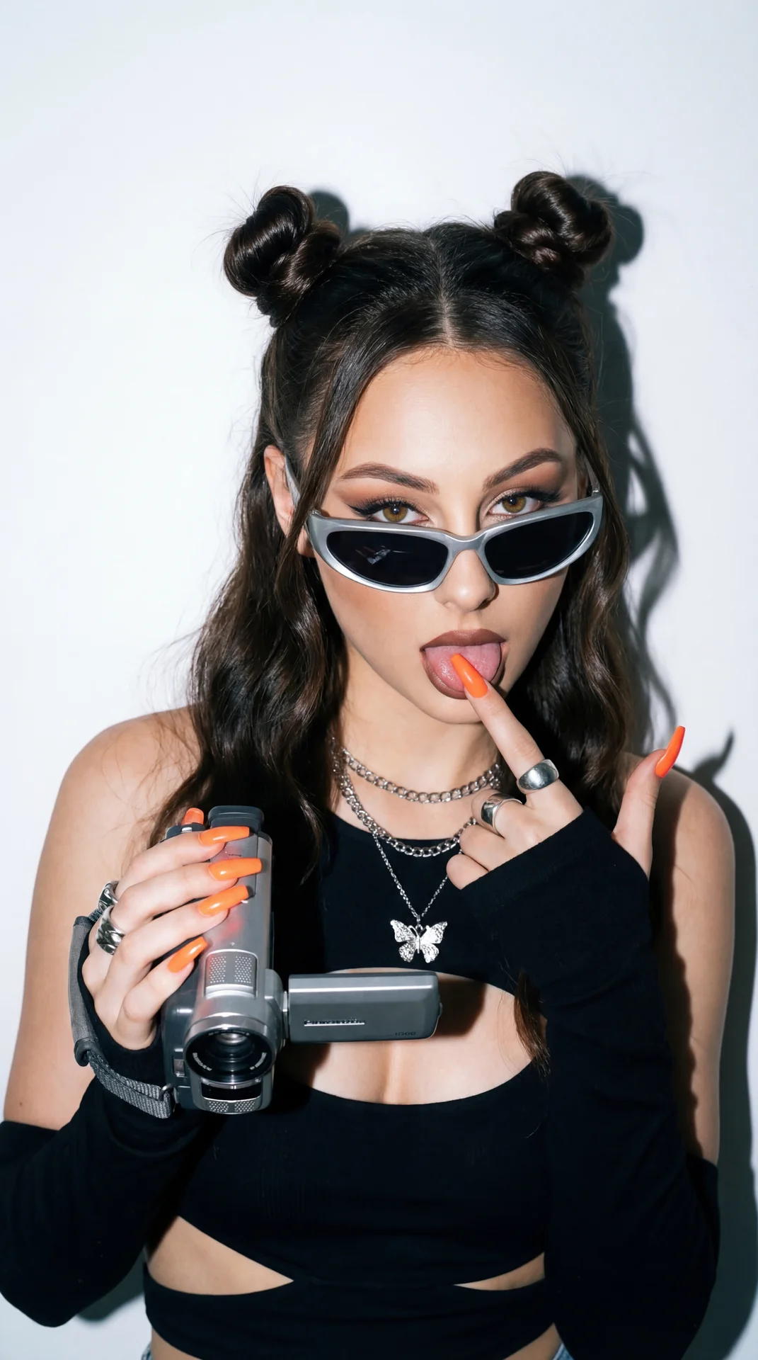A girl captured in a trendy, playful Y2K-aesthetic portrait shot with a vintage flash photography effect.

Pose and Hands: The girl is striking a cheeky pose facing the camera.
• Right Hand: Her right hand is raised to shoulder height, firmly gripping a s