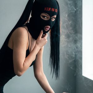 Фотосцена в том же образе референса: модель в чёрной вязаной маске-бини (лицо не видно), прическа: две высокие прямые чёрные хвостики, одежда: чёрный тонкий топ на тонких бретелях; локация: та же минималистичная студия с матовой светло-серой стеной, низки