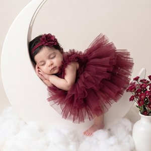 Professional studio newborn portrait, portrait orientation, full-body shot, slightly high angle, straight-on framing; sleeping baby on a matte white crescent-moon prop; side-lying fetal curl; head gently tilted forward to the left, eyes closed facing left