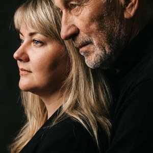 Сохрани лица людей с исходного фото 1:1, без изменений и искажения черт лица. Создай Вертикальный гиперреалистичный цветной портрет, крупный план: мужчина и женщина стоят в профиль, смотрят в одну сторону. Мужчина обнимает женщину сзади, его голова прижат