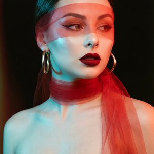A girl, medium close-up head-and-shoulders portrait, eye-level camera angle, professional DSLR studio photography. Slender figure. Standing with torso angled slightly forward-left, completely turning her head to gaze sharply off-camera to the right. Arms 