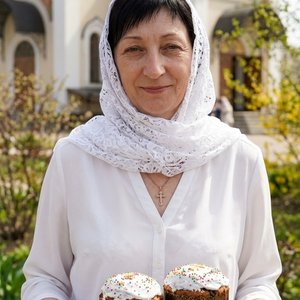 Точное воспроизведение внешности с загруженной фотографии: форма лица, особенности глаз, носа, губ, цвет и длина волос, идентичная структура лица, максимальное сходство. Фотореалистичный портрет по пояс, женщина стоит на фоне православной церкви в пасхаль