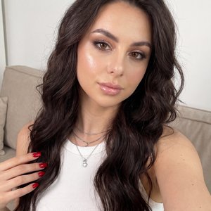 Raw photo, hyper-realistic, indistinguishable from a real photograph, ultra-high detailing, 8k resolution. Close-up first-person selfie perspective, arm extended out of frame, no phone visible. Indoor on a beige couch against a clean white wall, cozy mini