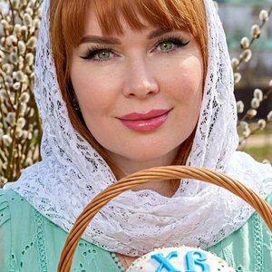 Потрясающий портрет крупным планом светлокожей женщины с эффектным макияжем, сосредоточенной и смотрящей прямо на зрителя. У нее темные волосы, эффектная крылатая подводка для глаз, длинные темные ресницы, идеально очерченные брови и полные блестящие розо