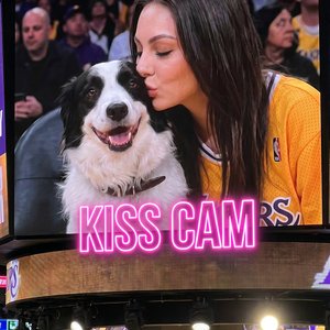 Ultra-realistic NBA jumbotron kiss cam screenshot, identity preserved exactly from reference image.

Young woman sitting at a Lakers playoff game shown on the giant arena screen during a kiss cam moment. Camera is closer to the jumbotron so her face is cl