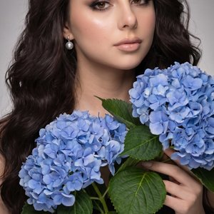 The studio portrait shows a close-up of a young woman of European descent, with her hair falling over one shoulder in soft, voluminous curls. She is looking directly at
the camera, with a gentle half-smile, showcasing her high cheekbones, which are accent