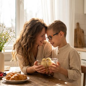 Фотореалистичное изображение, вертикаль 9:16, домашняя съёмка на кухне, ❗️ABSOLUTE IDENTITY LOCK 1:1 — сохранить внешность женщины и ребёнка без изменений, композиция строго: женщина и ребёнок сидят рядом за деревянным столом, наклонены друг к другу, лбы 
