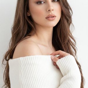 Professional studio portrait, medium close-up (head-and-shoulders), eye-level camera, slight three-quarter angle; indoor minimalist setting with a seamless white wall; high-key look, soft diffused light from camera-left with gentle fill from right, shallo