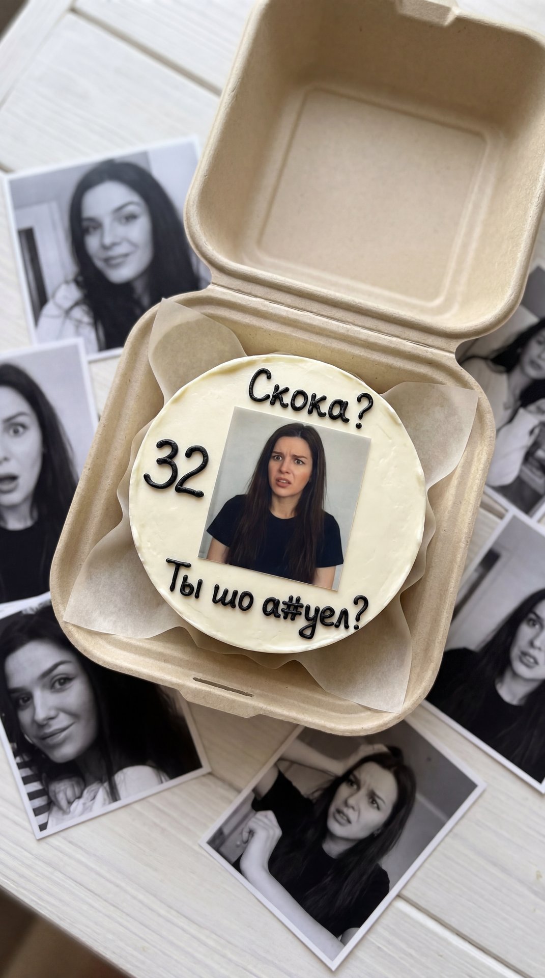 Создай реалистичный портрет, не меняя черты лица,не меняй цвет волос.Реалистичная фотография в стиле флэтлэй (вид сверху под небольшим углом), запечатлевшая открытую биоразлагаемую крафтовую коробку-ракушку, стоящую на белом деревянном столе поверх разлож