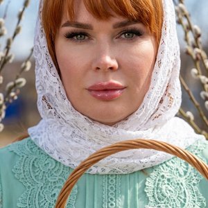 Потрясающий портрет крупным планом светлокожей женщины с эффектным макияжем, сосредоточенной и смотрящей прямо на зрителя. У нее рыжие  волосы, , длинные темные ресницы, идеально очерченные брови и полные блестящие розовые губы. Ее глаза очаровательного с
