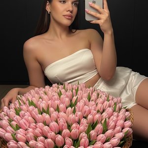 Cinematic mirror selfie of the same woman \(не менять лицо, волосы\)\. Она полулежит, опираясь головой на огромный букет розовых закрытых тюльпанов в корзине \(их примерно 3000 штук\), полностью заполняющий передний план\.
Поза: одна рука поднята с iPhone