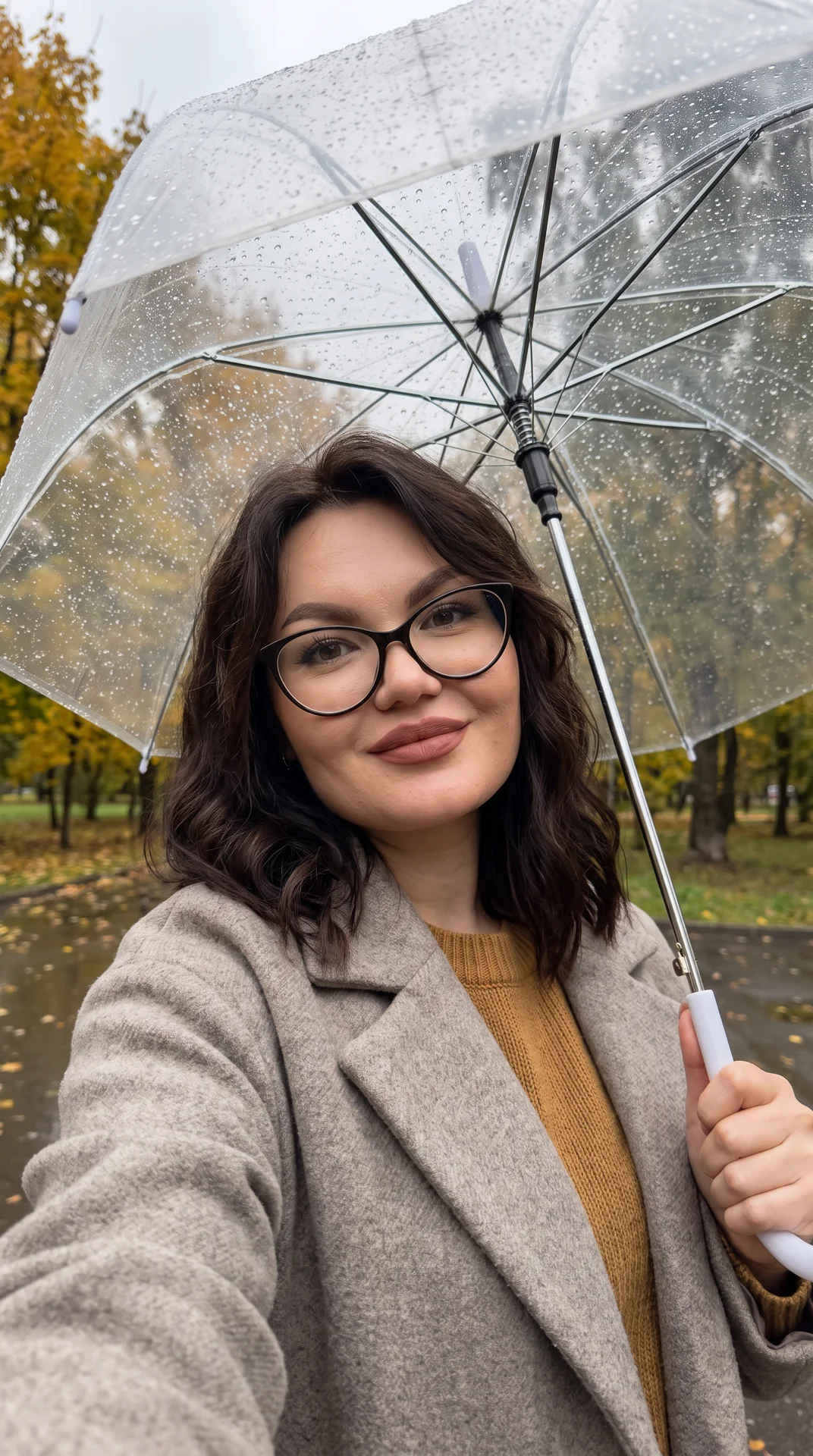 Максимально фотореалистичное селфи на iPhone 17 Pro Max, вертикальный кадр 9:16, снято с вытянутой руки во время прогулки под дождём. Камера расположена немного ниже уровня глаз и направлена слегка снизу вверх, широкоугольная перспектива смартфона. В кадр