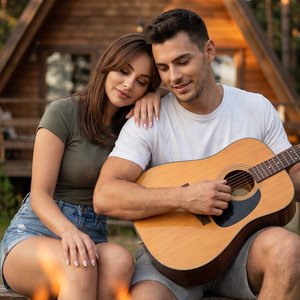 Hyperrealistic vertical 9:16 photo, pro DSLR (85mm f/1.8) eye‑level medium-close shot: couple sitting on a bench in front of a wooden A-frame cabin at golden hour; preserve original hairstyle and facial features (do not alter). Woman leaning her head on h