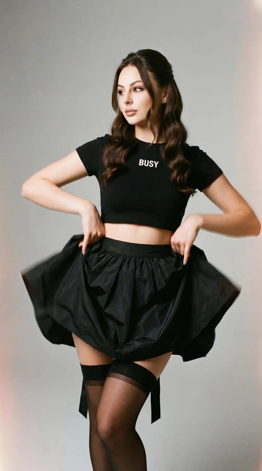 A girl in a minimalist studio on a smooth gray background, shot with a professional camera; full-length shot (from the middle of the thigh and above), a small low angle, three-quarter view; stands with her body weight on her right leg, hips slightly shift