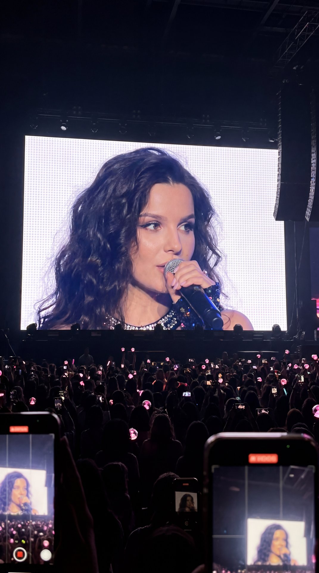 1 portrait photo of a person [MAIN TASK - "REALISTIC JUMBOTRON TRANSLATION AT A K-POP CONCERT"] Transform the person in the photo into a famous K-pop artist performing at a sold-out concert. The final result should look like this: a real fan secretly take