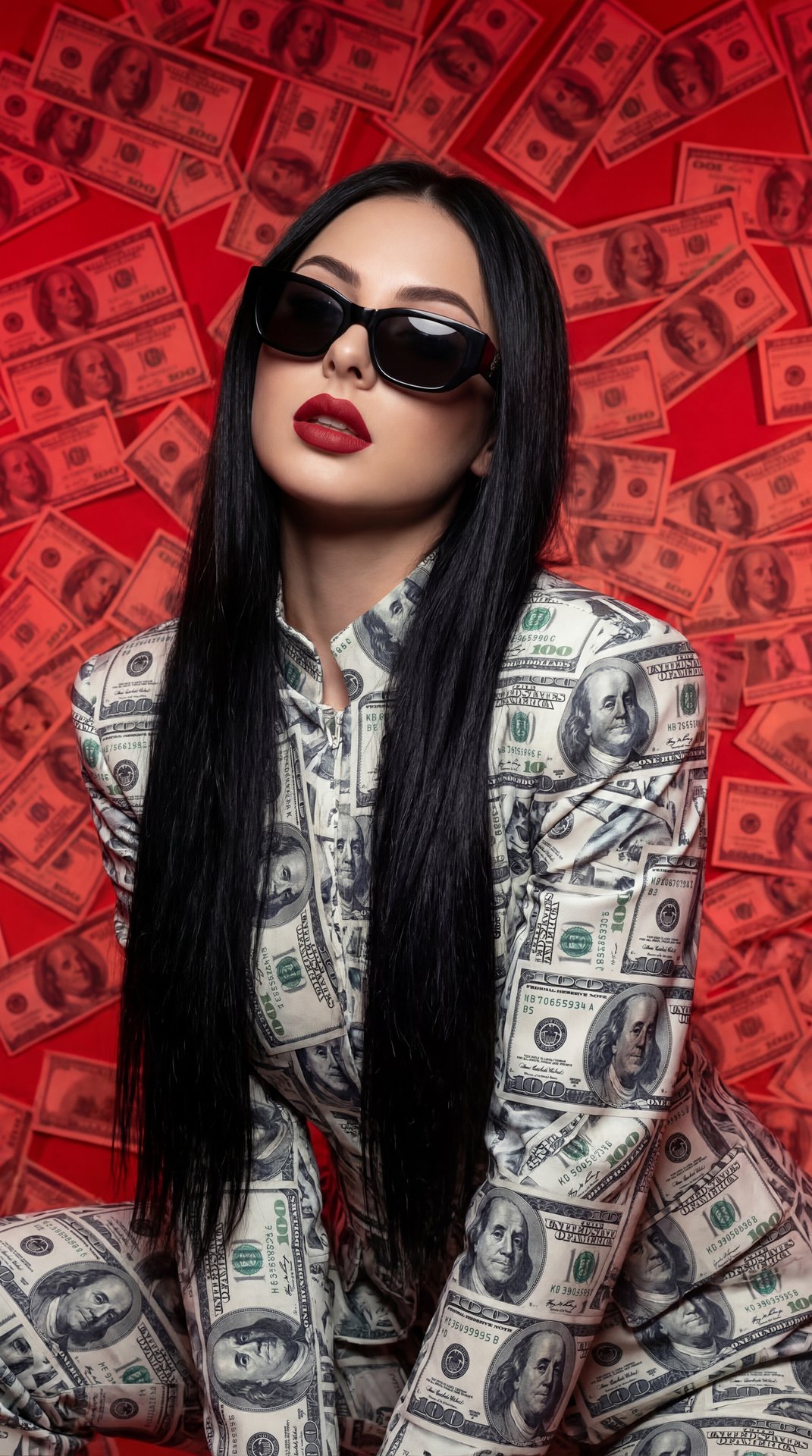 A girl is posed confidently in front of an intense red background covered with overlapping images of U.S. dollar bills, creating a striking, high-contrast atmosphere. She stands or leans slightly forward, with her shoulders at a slight angle to the camera