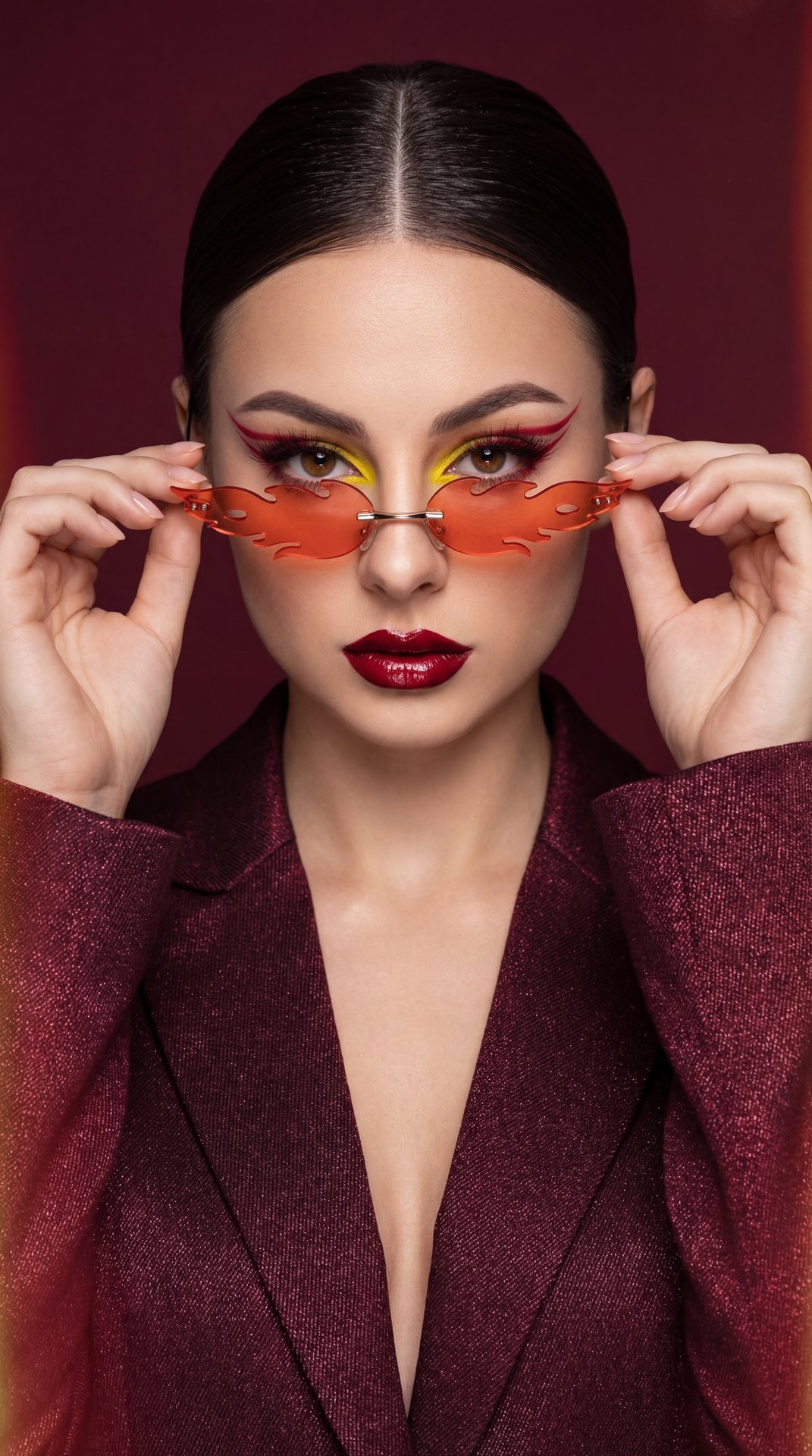 A girl, medium close-up shot, eye-level camera angle, professional high-fashion studio photography. Slender figure. Shoulders squared forward, head tilted slightly down. Gaze locked piercingly directly into the camera over the rims of lowered sunglasses. 