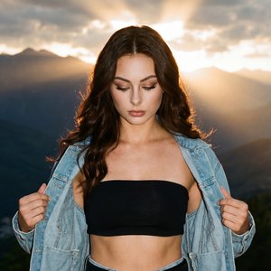 A girl stands outdoors in front of a dramatic mountainous landscape during sunset, with warm rays of light breaking through clouds behind her, creating a striking and serene atmosphere. She is posed facing slightly downward with her head tilted forward, h