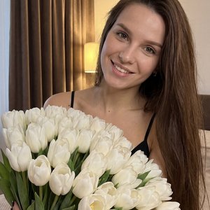 На этой фотографии запечатлена молодая женщина в уютной домашней обстановке, держащая в руках огромный букет цветов.
Главный герой и композиция
• Центральный объект: Девушка с длинными прямыми шоколадными волосами по пояс . Она слегка наклонила голову к п