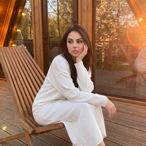Hyper-realistic authentic raw photograph, completely indistinguishable from reality, unretouched lifestyle capture. Medium-full (three‑quarter) shot, slightly low eye‑level, three‑quarter side angle from the subject’s right; a woman seated sideways on a s