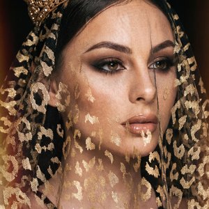 A girl in a regal, spectacular studio portrait wearing a crown of gold filigree and a transparent tulle veil with a leopard print, completely covering her head and face; close-up shot (head and shoulders), 3/4 angle of the girl, at eye level; hands not vi
